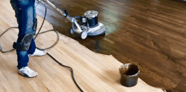 Spreading stain on a hardwood floor with a machine.